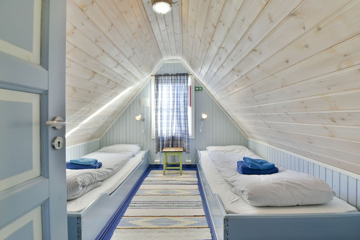 Ein kleines, gemütliches Schlafzimmer im Dachgeschoss mit zwei Etagenbetten, Holzbalkendecke und einem Fenster mit Vorhängen.