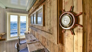 Un intérieur en bois avec une table en bois, des chaises, un gouvernail de bateau et une fenêtre donnant sur la mer.