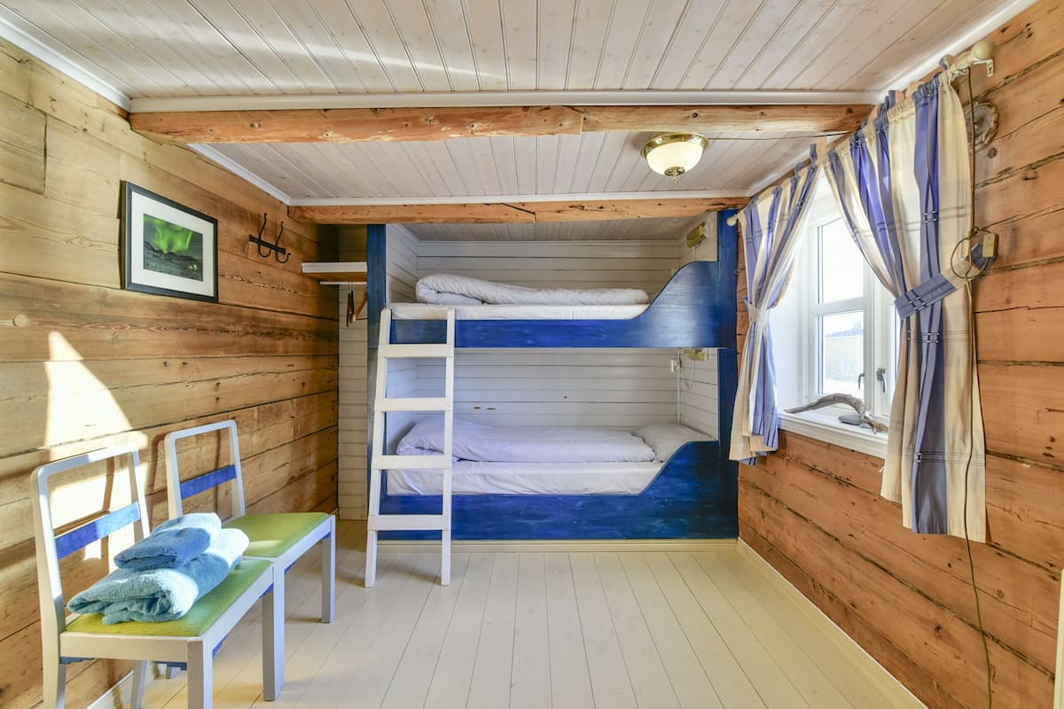 Eine Holzhütte mit Stockbetten, einer Leiter, einer Bank und einem Fenster mit Vorhängen.