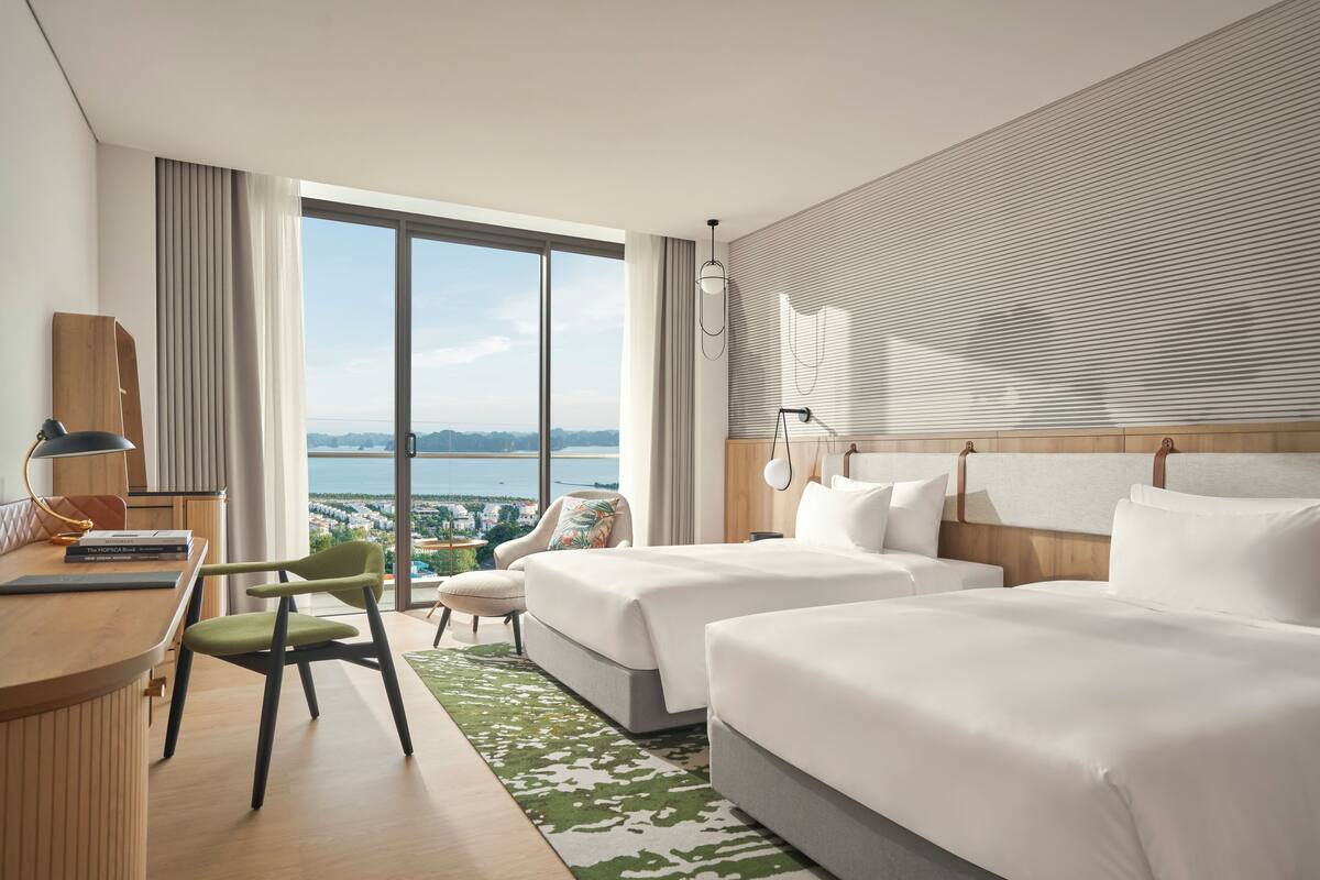 Habitación de hotel con dos camas, un escritorio, una silla y vista al mar.