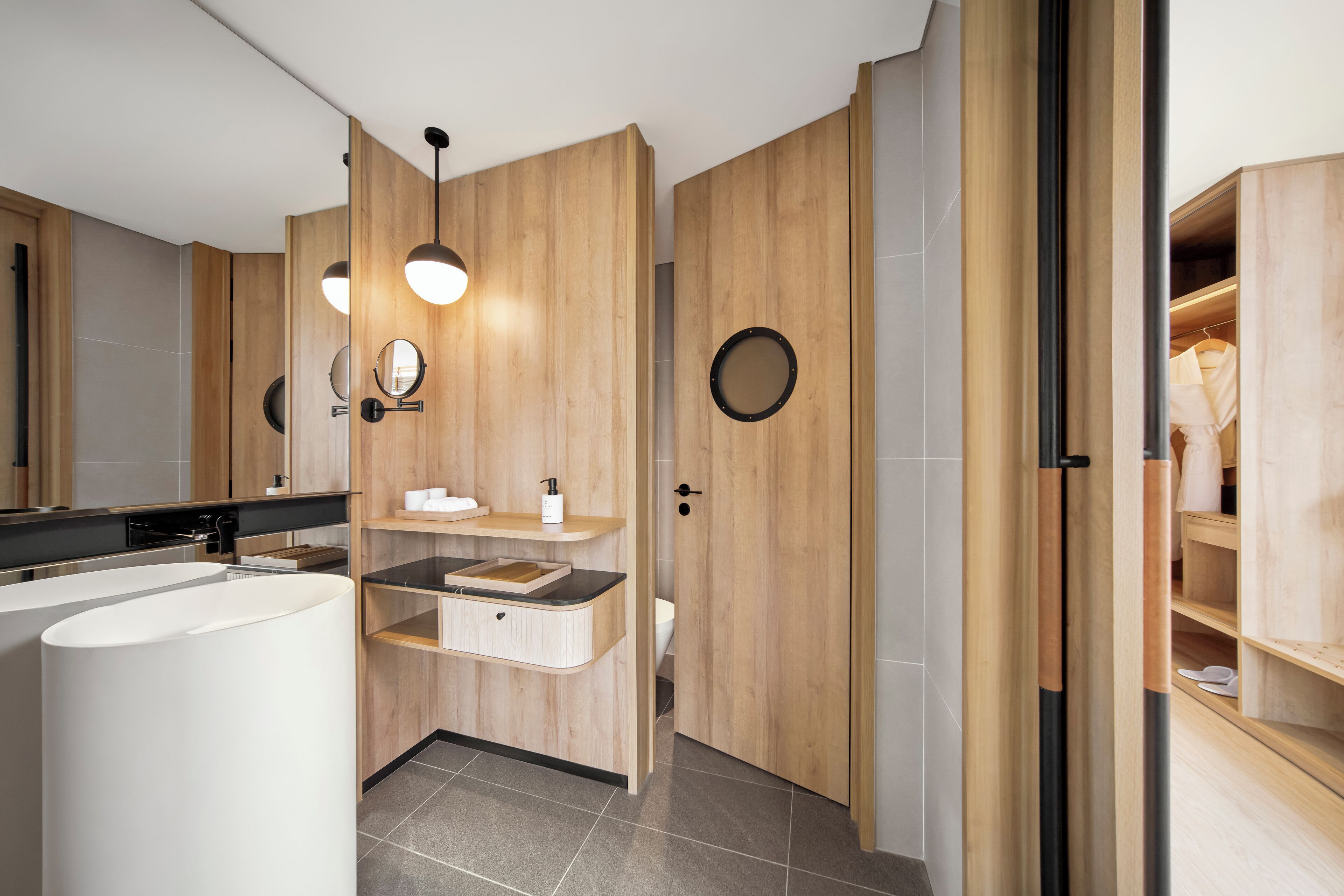 A modern bathroom with a large white sink, wooden vanity, and a round mirror.