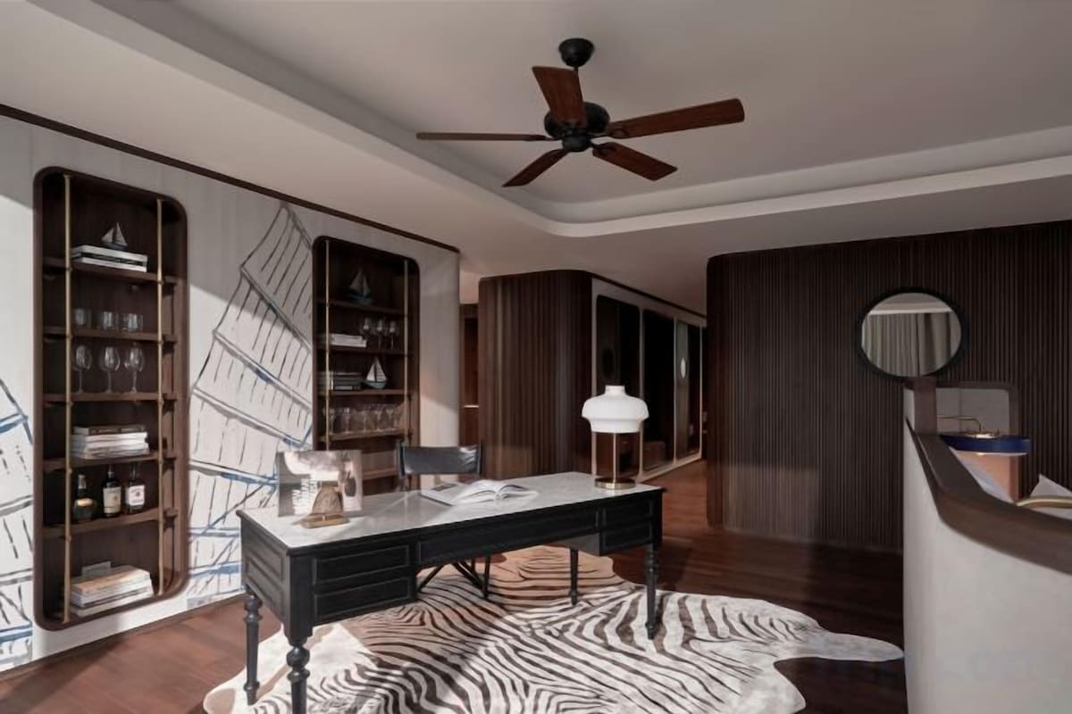 A room with a desk, bookshelves, a ceiling fan, and a patterned rug.