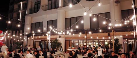 Un área de comedor al aire libre con guirnaldas luminosas y varias mesas y sillas.