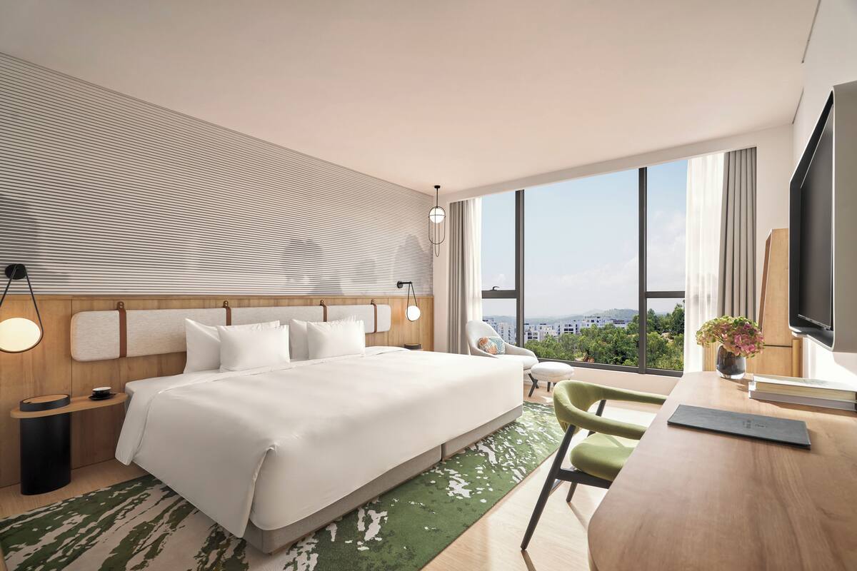 Una habitación de hotel moderna con una cama grande, un escritorio, una silla y vistas a la ciudad.