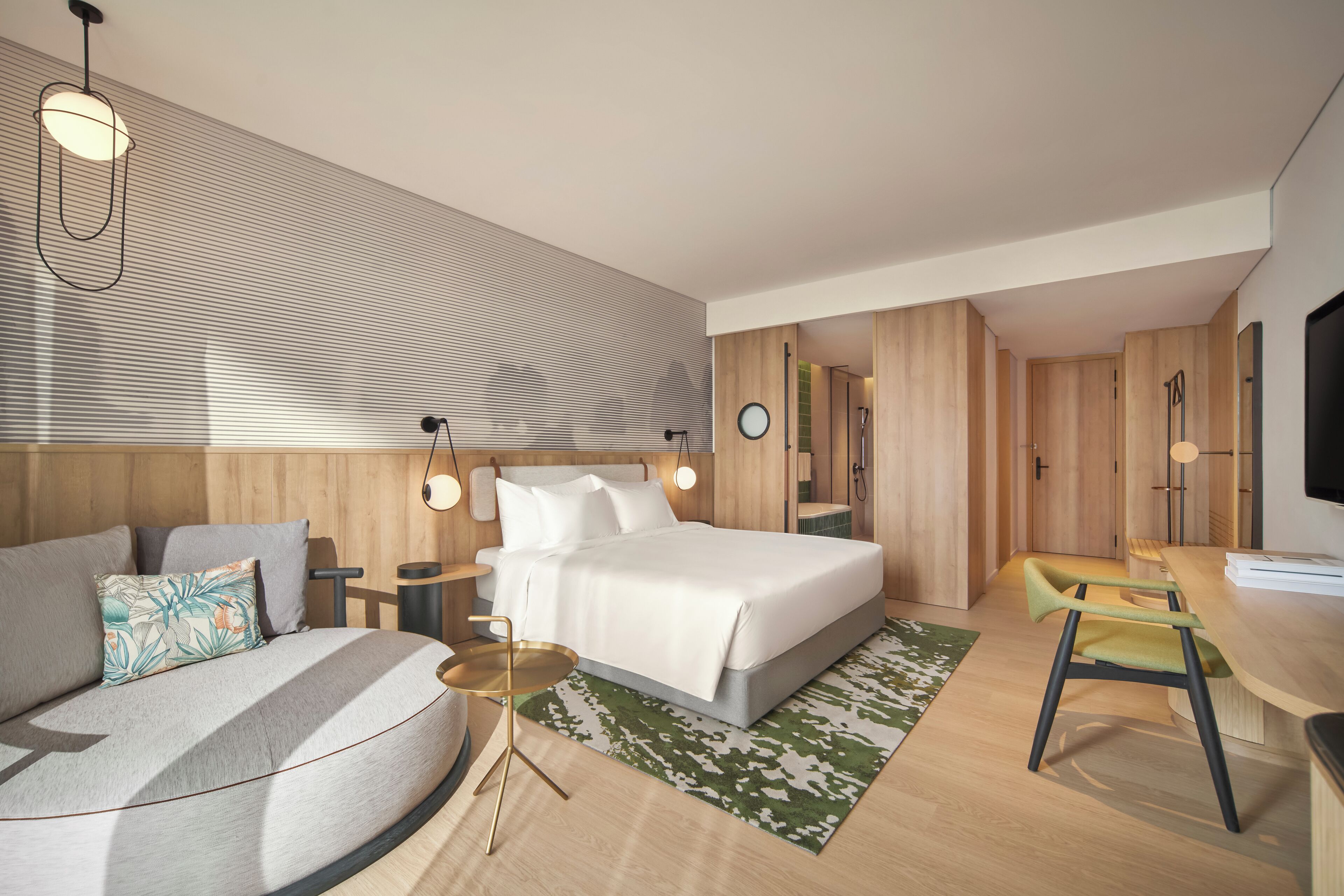 A modern hotel room with a bed, a sofa, a desk, and a TV.