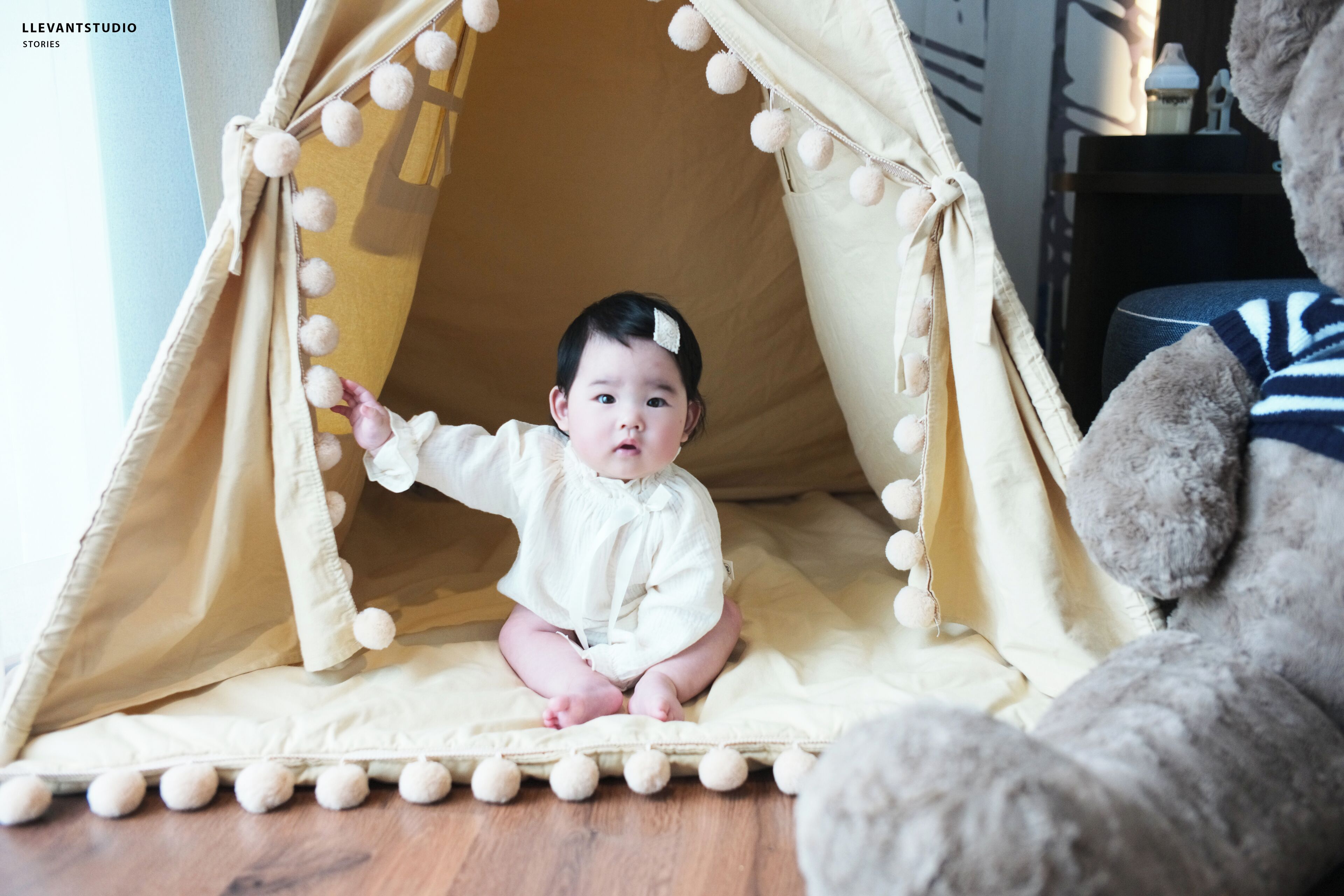 A child sitting inside a tent-like structure with pom-poms on the edges.