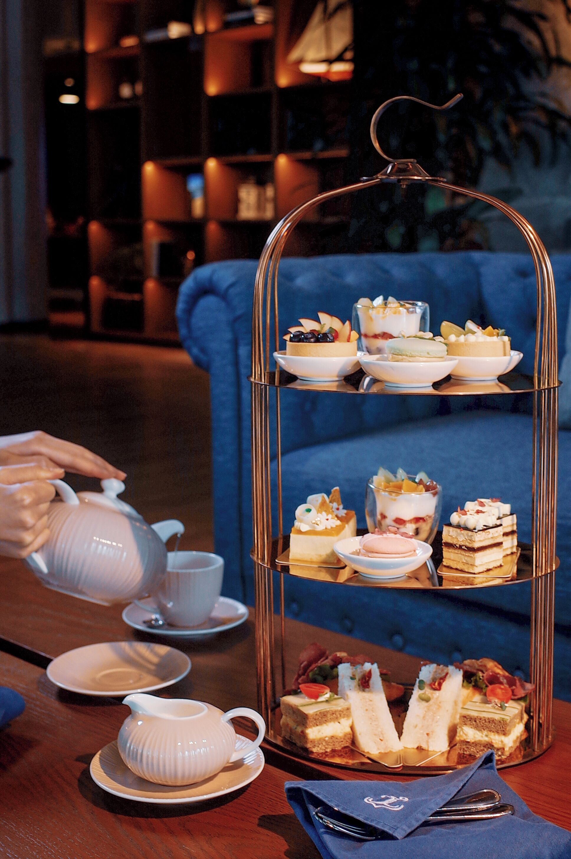 A tiered dessert stand with various pastries and a teapot on a table.