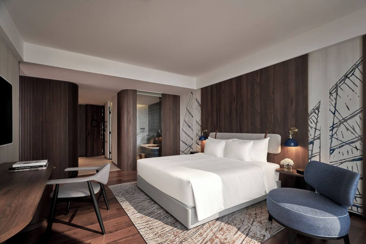 Habitación de hotel moderna con una cama grande, un escritorio con una silla, un televisor y un baño visible a través de una puerta abierta.