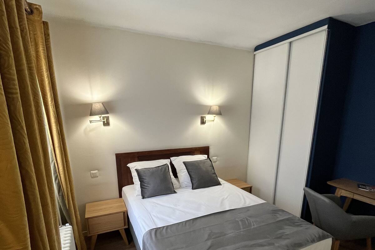 A hotel room with a bed, bedside lamps, a desk, and a chair.