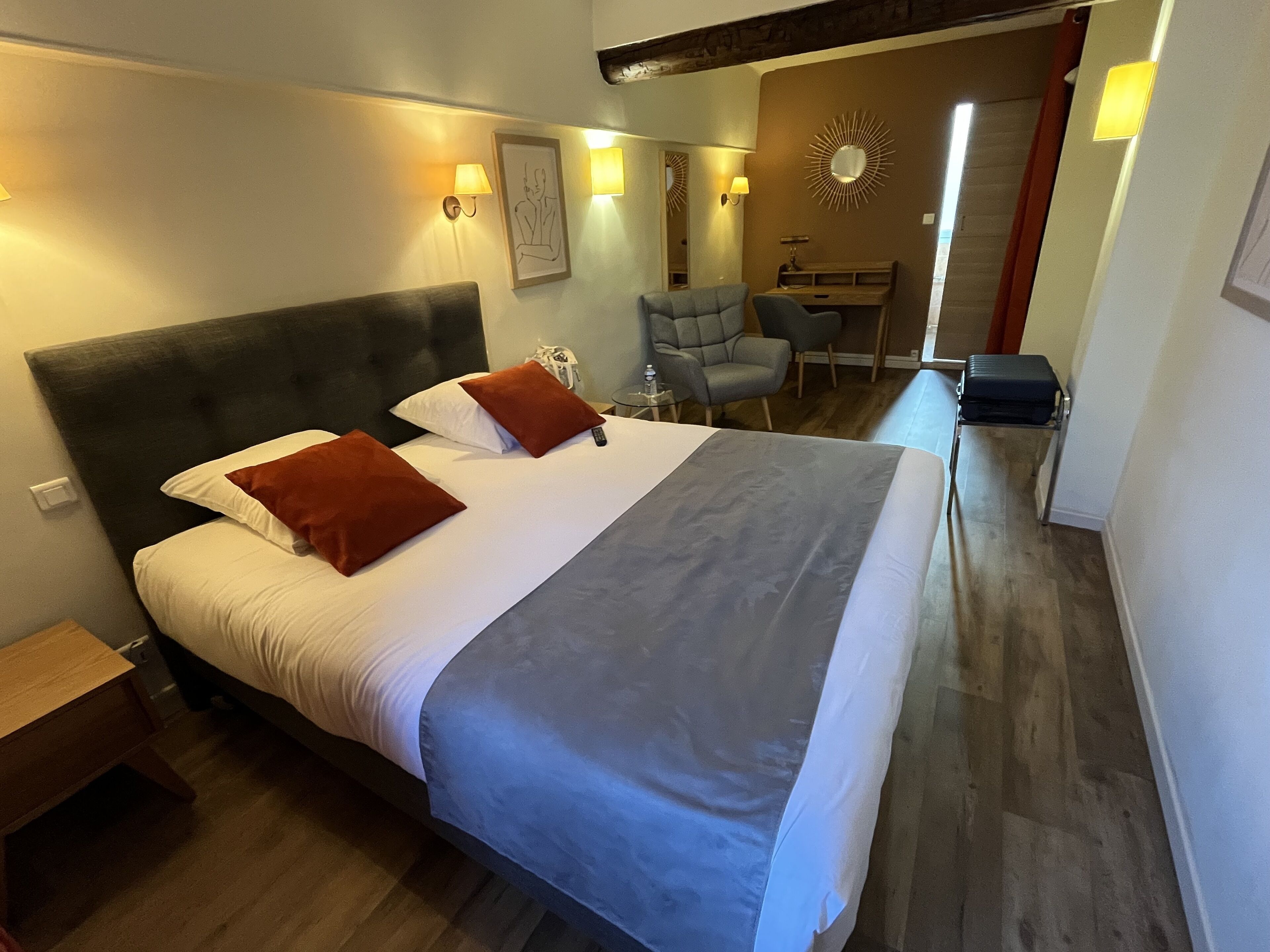 Une chambre d’hôtel avec un grand lit, un bureau, une chaise et un miroir au mur.
