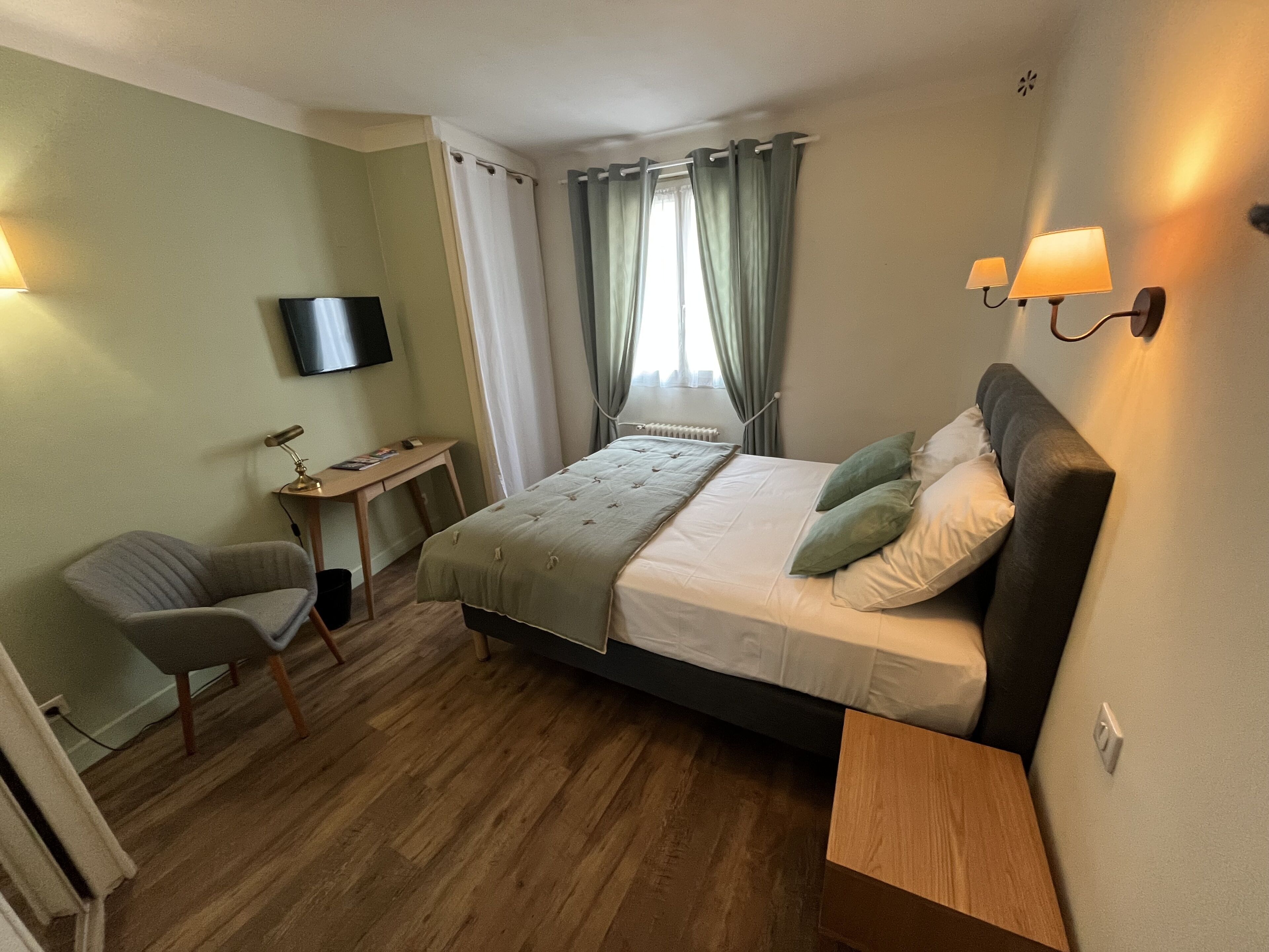 Habitación de hotel con cama, escritorio, silla, televisor y ventana con cortinas.