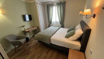 Habitación de hotel con cama, escritorio, silla, televisor y ventana con cortinas.