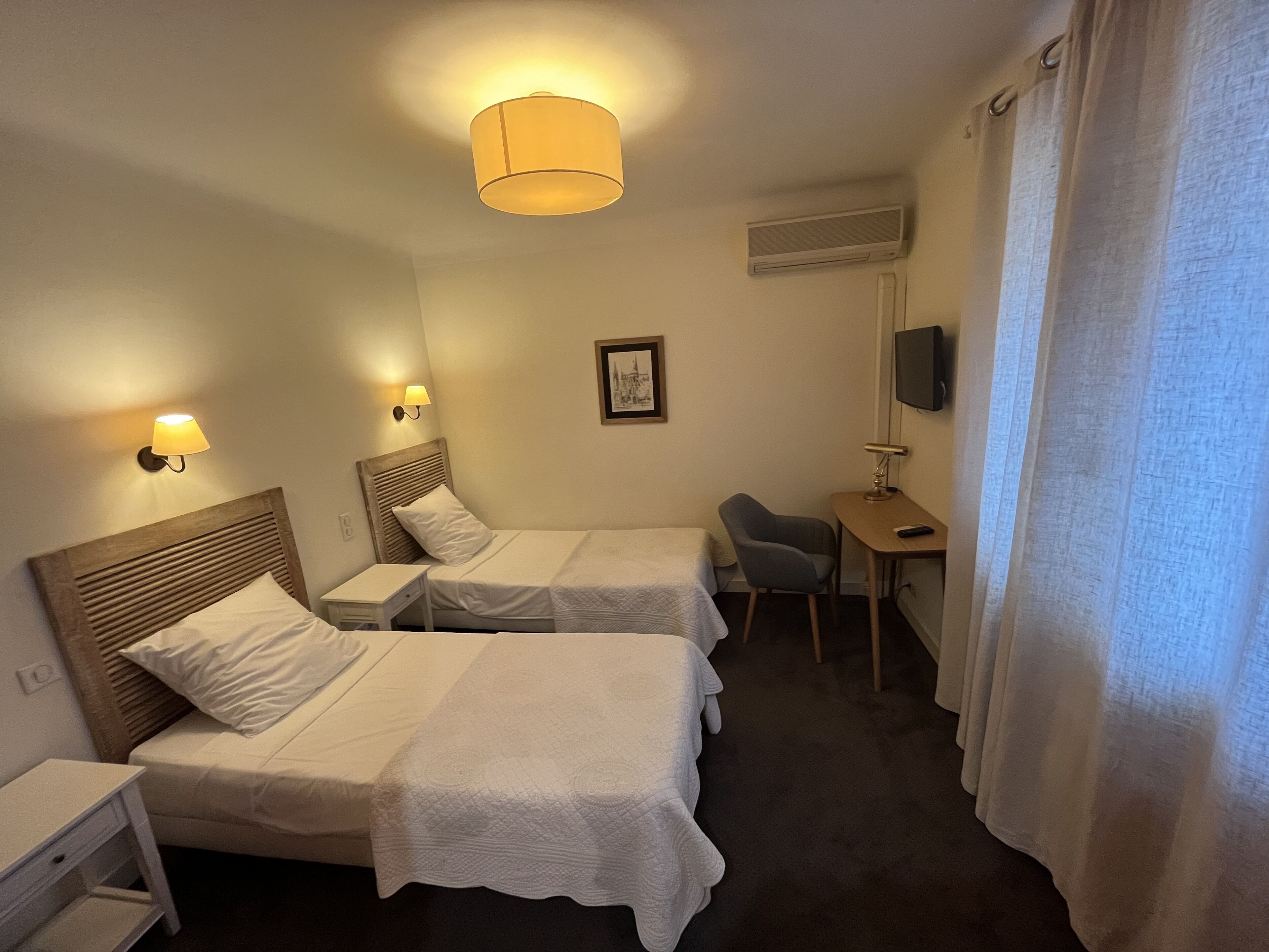 A hotel room with two beds, a desk, a chair, a TV, and a lamp.