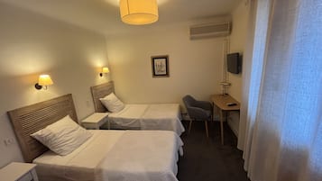A hotel room with two beds, a desk, a chair, a TV, and a lamp.