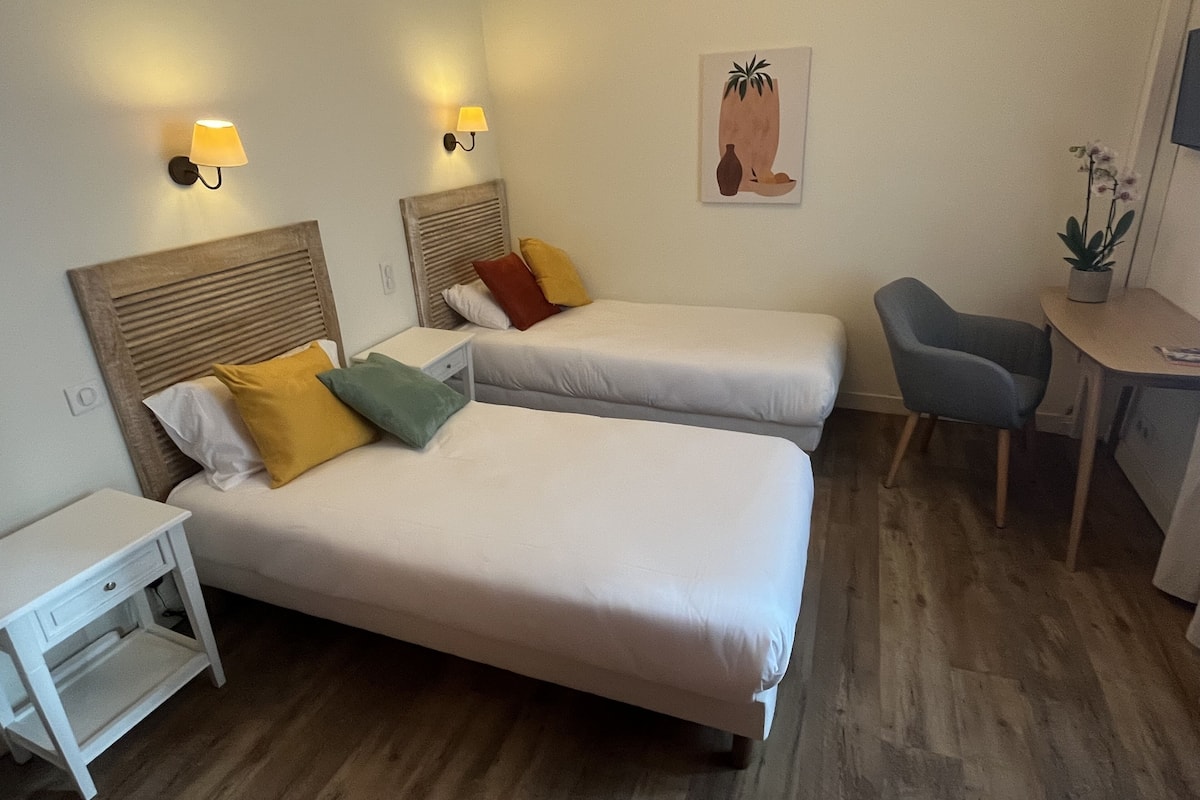 A hotel room with two beds, a desk, a chair, and a small table.