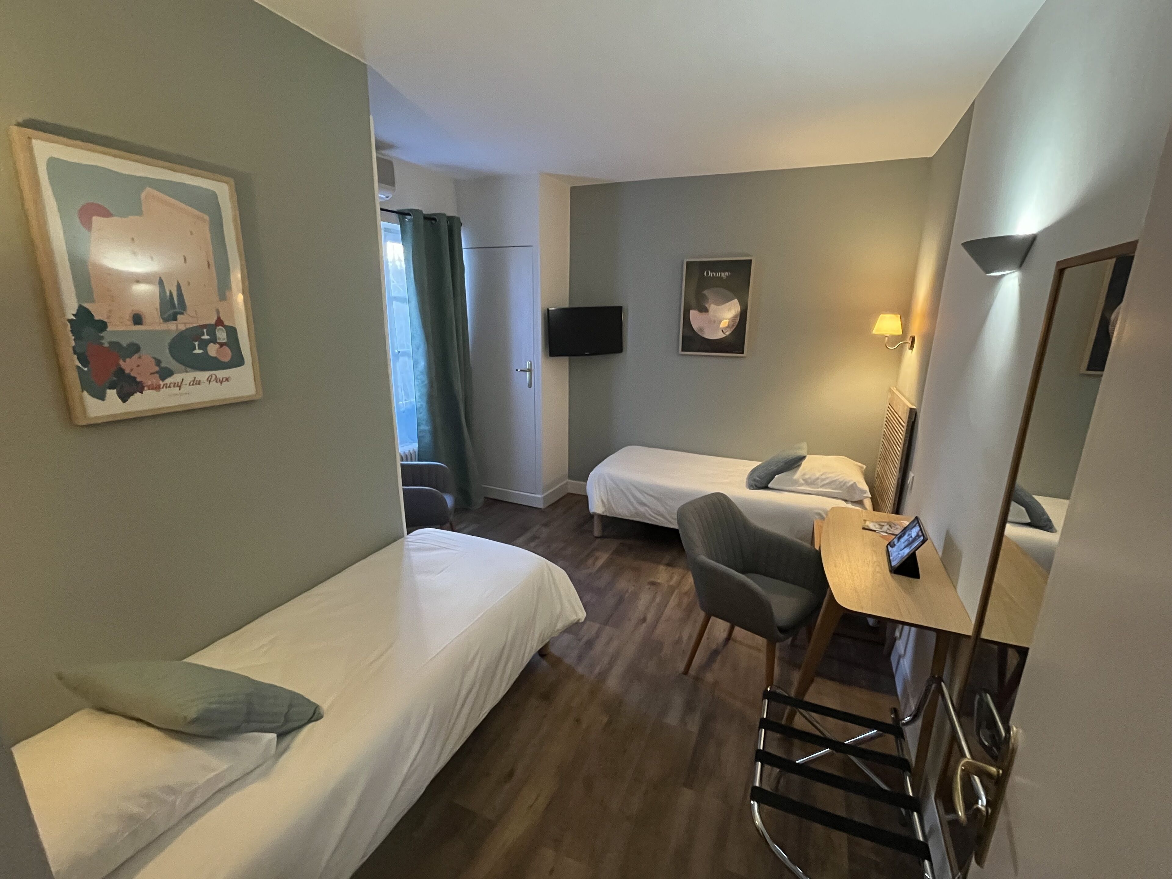 A hotel room with two single beds, a desk with a chair, a flat-screen TV, and a mirror.