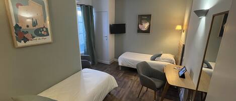 A hotel room with two single beds, a desk with a chair, a flat-screen TV, and a mirror.