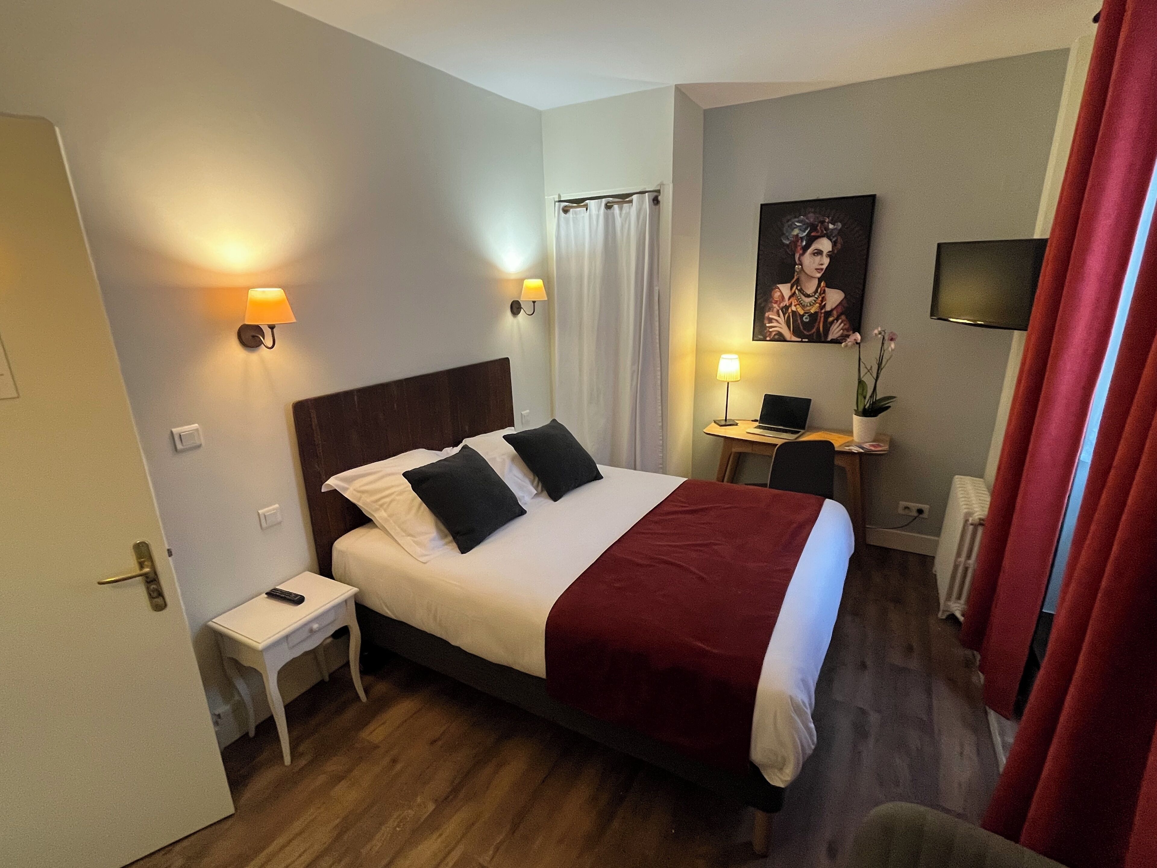 A hotel room with a bed, bedside table, lamp, desk, chair, and a television.