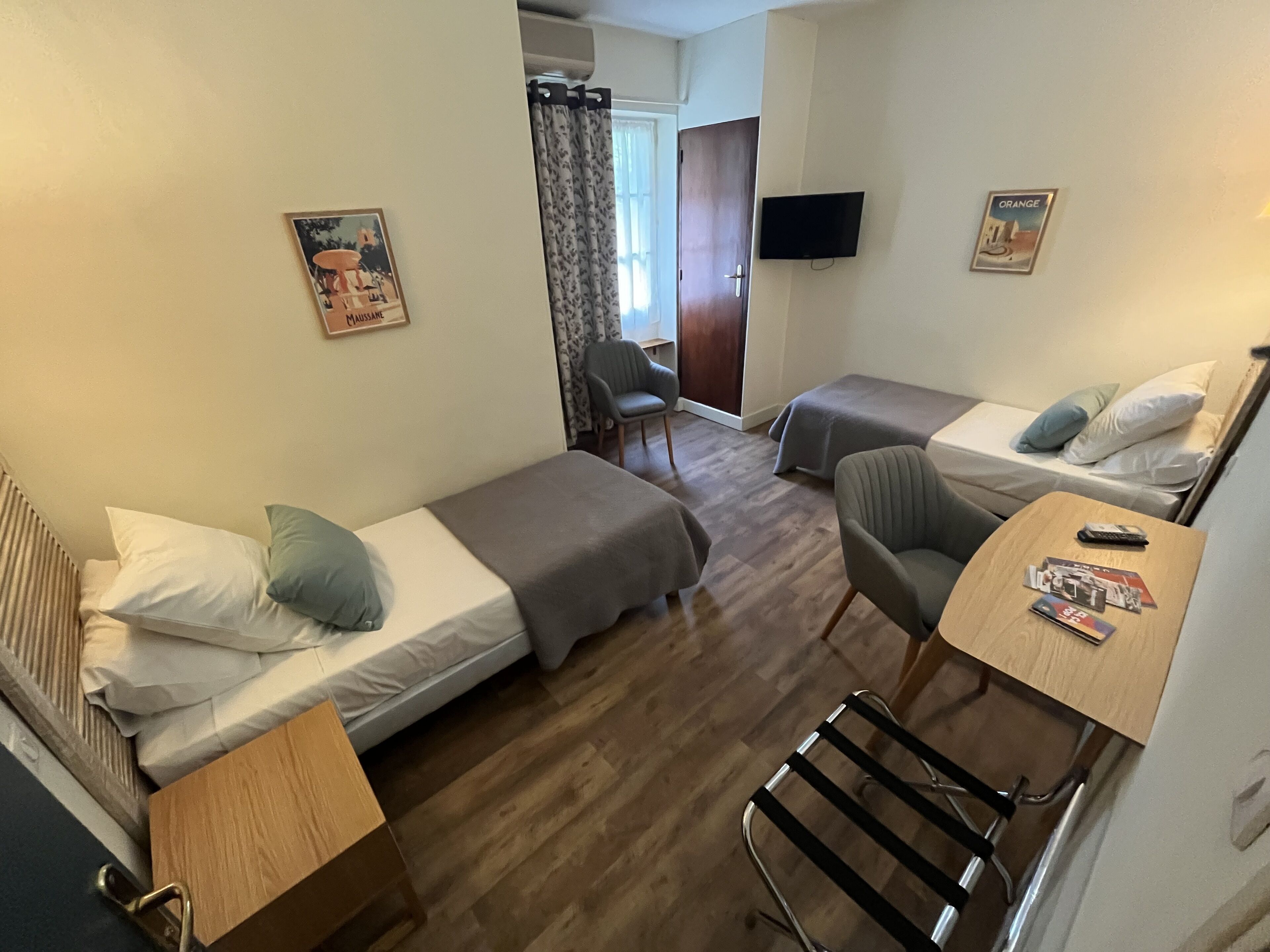 Habitació d'hotel amb dos llits individuals, una taula amb una cadira, un televisor i una porta que condueix a una altra habitació.