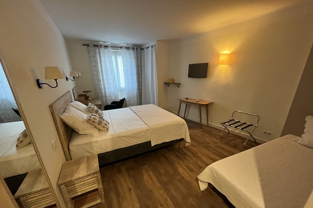 A hotel room with two beds, a desk, a chair, a TV, and a lamp.