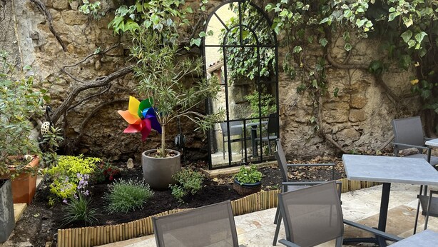 Un patio al aire libre con suelo de piedra, sillas de metal, una planta en maceta y un molinillo de viento.