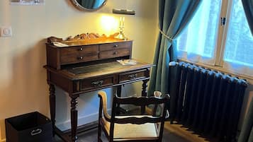 Et træbord med et spejl, en lampe og en stol i et rum med trægulv og et vindue med gardiner.