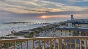 A beach view with a pier, beach umbrellas, and buildings along the shore.