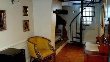 Una habitación amplia con piso de madera, una escalera y una silla.