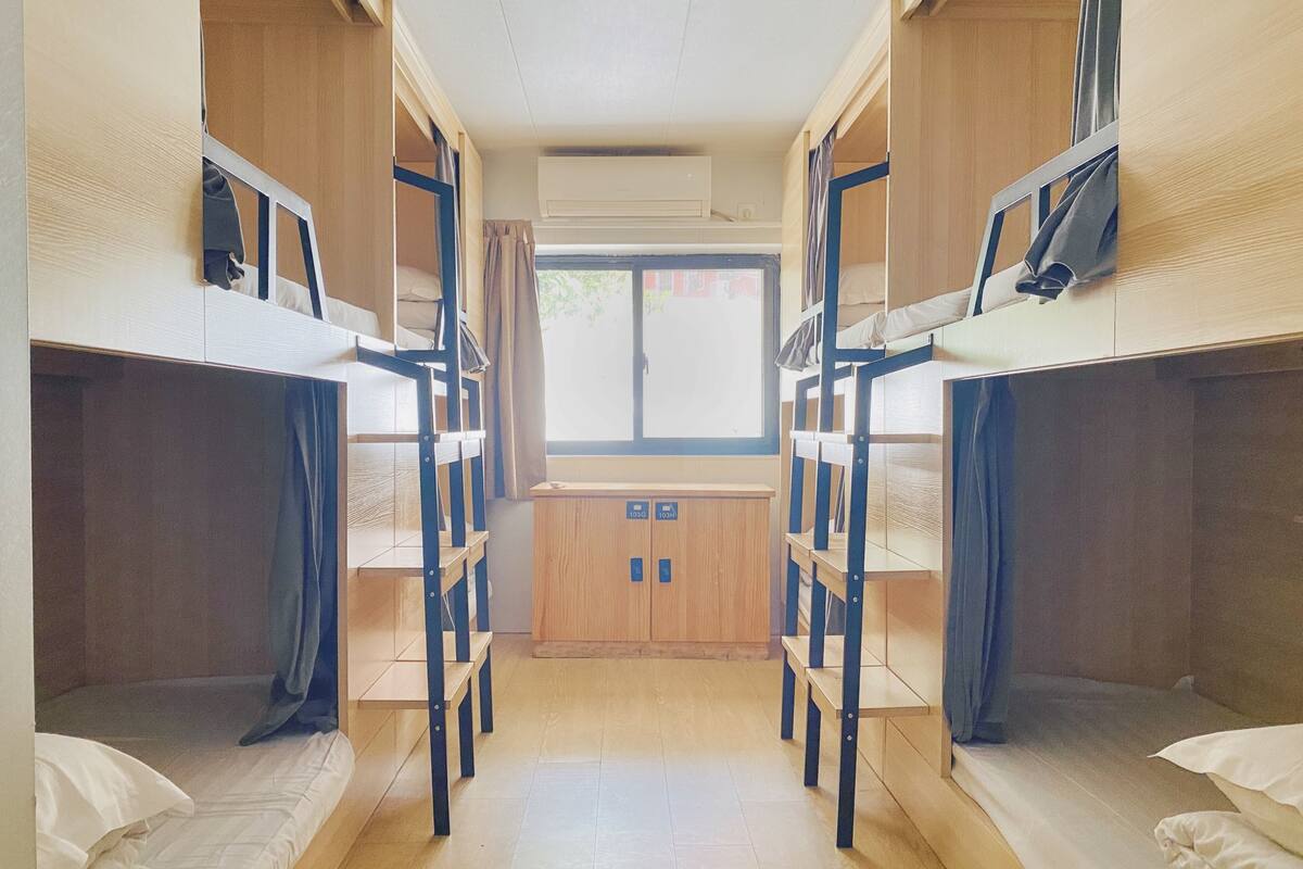 Une chambre de dortoir avec des lits superposés, une fenêtre et une armoire en bois.