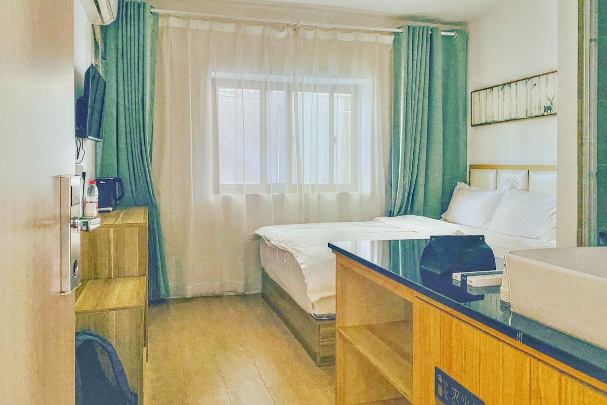 Une chambre d’hôtel équipée d’un lit, d’un bureau, d’une chaise, d’une télévision et d’une fenêtre avec des rideaux.
