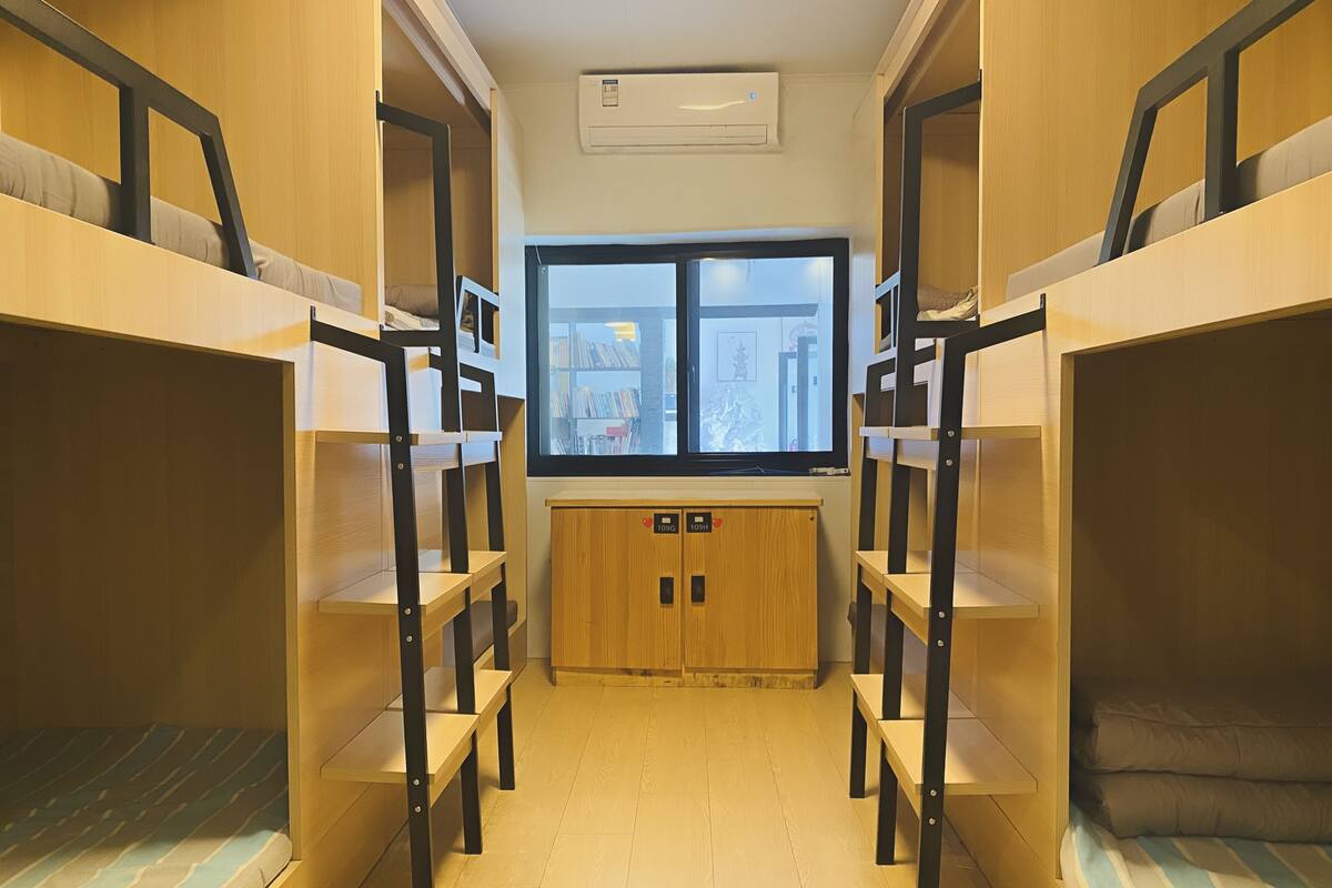 Une chambre avec des lits superposés en bois, une fenêtre donnant sur la ville et un petit meuble avec des casiers.