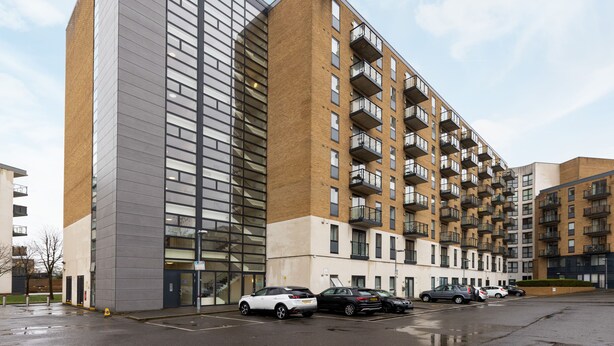 A multi-story residential building with a modern design, featuring balconies and a parking lot with several cars. - The Wimbledon Collection (London)