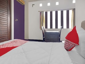 Una habitación de hotel con cama, ventana con cortinas, una silla y una pequeña mesa.