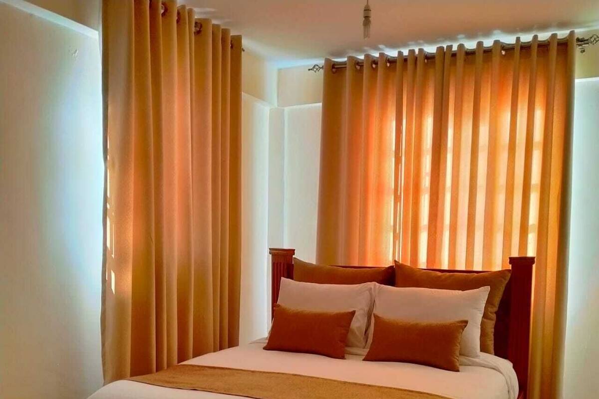 Cama bem arrumada com estrutura de madeira e roupa de cama branca, acompanhada por dois travesseiros.