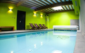 Une piscine avec un banc et des chaises longues, une porte et un plafond orné de poutres en bois et de luminaires.