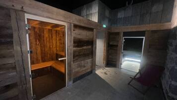 Een houten sauna met een bank, een stenen vloer en een glazen deur naar een betegeld gedeelte.