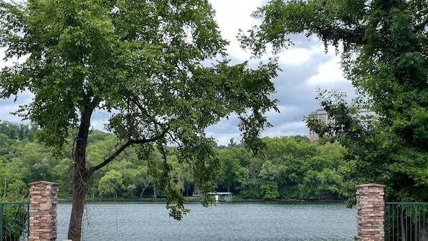 Une piscine bordée de piliers en pierre, entourée d’une végétation luxuriante et donnant sur un lac.