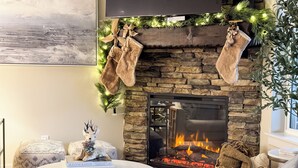 Un salon chaleureux avec une cheminée en pierre, un téléviseur à écran plat fixé au mur et des décorations de Noël festives.