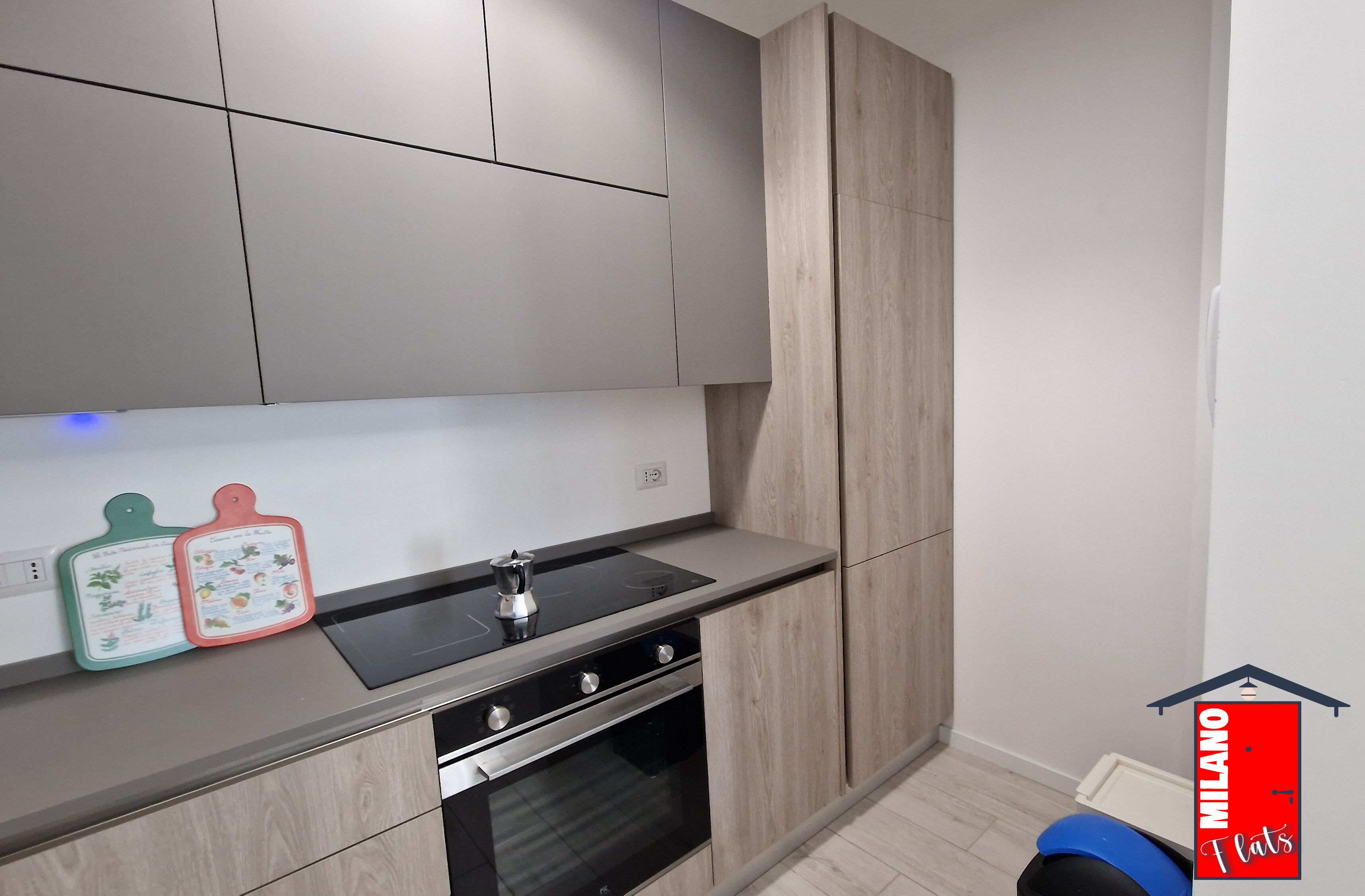 Une cuisine moderne avec des meubles gris, une plaque de cuisson à induction noire et un four encastré.