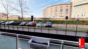 Un espace de stationnement avec plusieurs voitures, un bâtiment en arrière-plan et un panneau indiquant « MILANO Flats ».