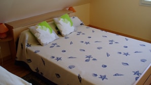 A bed with a white and blue patterned bedspread, two pillows with green and white designs, and a wooden headboard. - Propriété (Saint-Pierre-Quiberon)