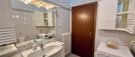 A modern bathroom with a marble sink, a large mirror, a wooden door, and a towel rack.