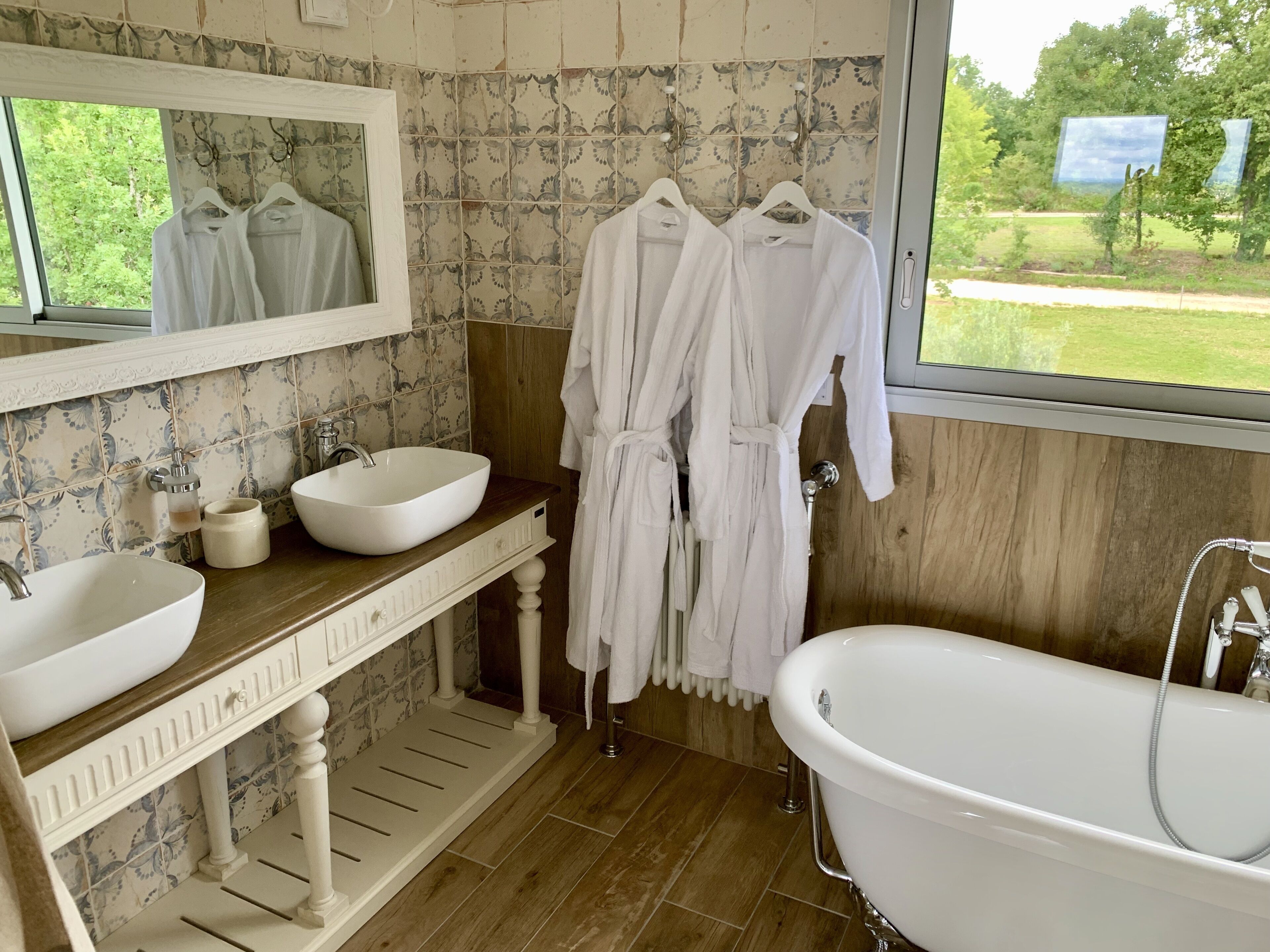 Une salle de bain avec un meuble-lavabo en bois, deux vasques, une baignoire et un grand miroir.