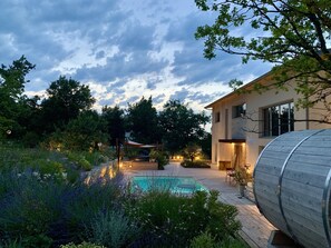 Une maison moderne avec une piscine, entourée d’une végétation luxuriante et sous un ciel nuageux.
