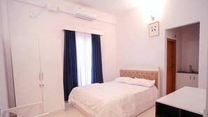 A bedroom with a bed, a wardrobe, a desk, and a kitchenette. - Kailath Safe Stay Tourist Home (Tiruvalla)
