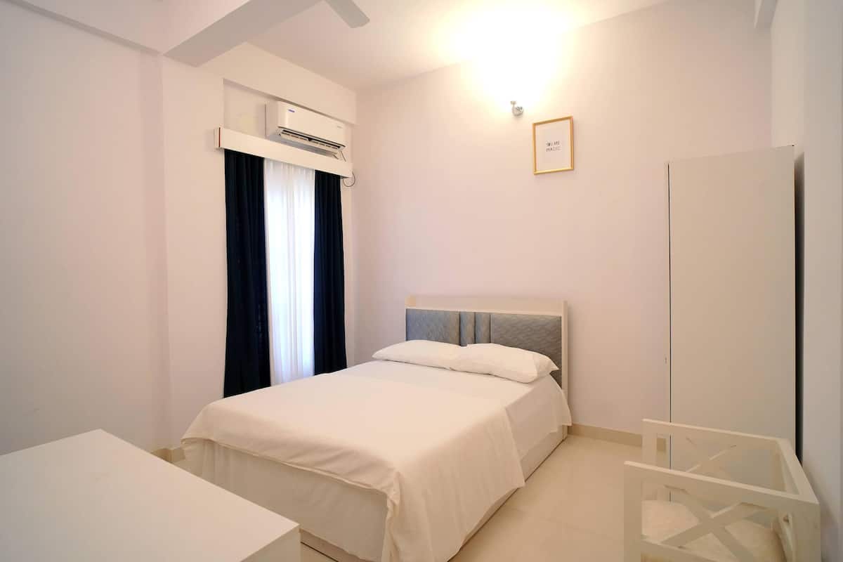 A bedroom with a bed, bedside table, wardrobe, and an air conditioning unit.
