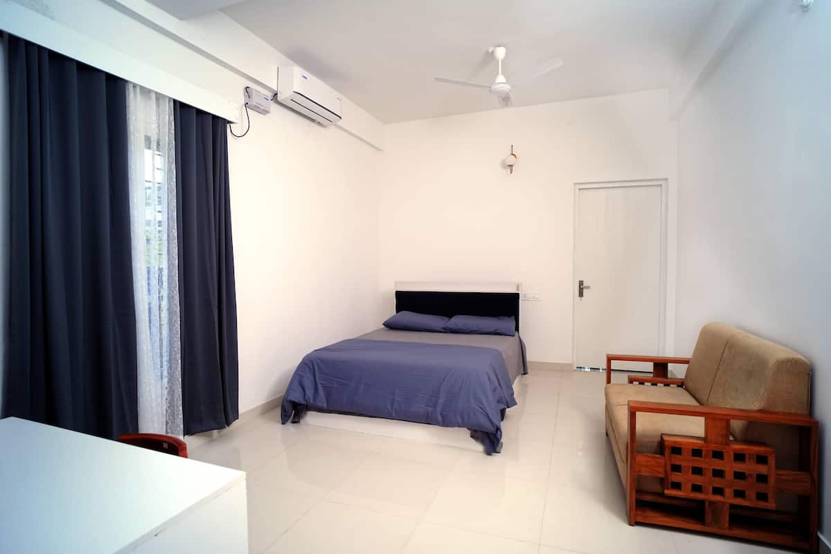 A bedroom with a bed, a wooden chair, a desk, and a ceiling fan.