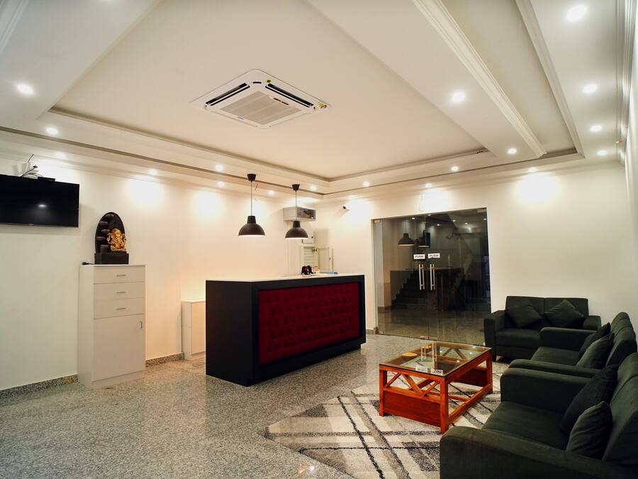 A modern living room with a red accent wall, a black sofa, a glass coffee table, and a flat-screen TV mounted on the wall.