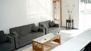 A modern living room with a grey sofa, a glass coffee table, and a small side table with a vase. - Kailath Safe Stay Tourist Home (Tiruvalla)