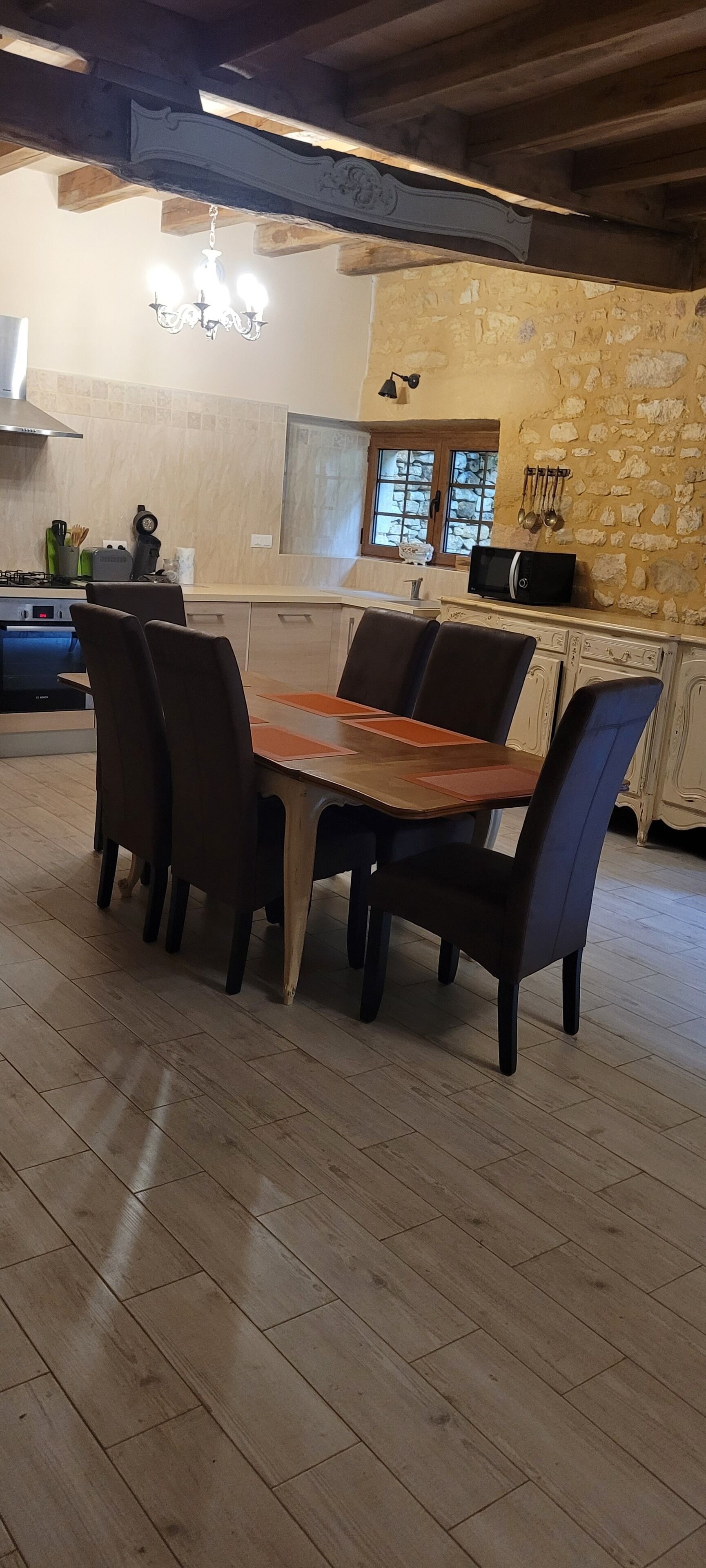 Ein Essbereich mit Holztisch und Stühlen, einer Steinwand und einer Küche im Hintergrund.
